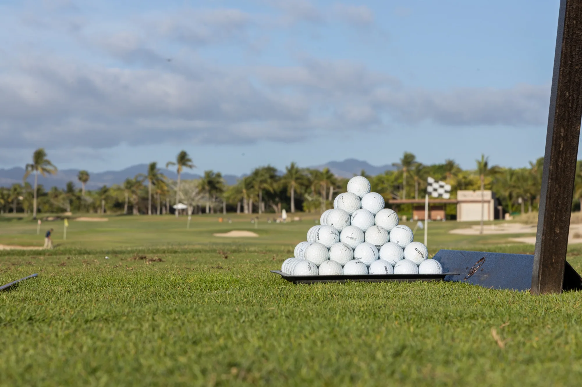 A pyramid of range balls on the practice facility at Punta Mita, with the course and mountains behind.